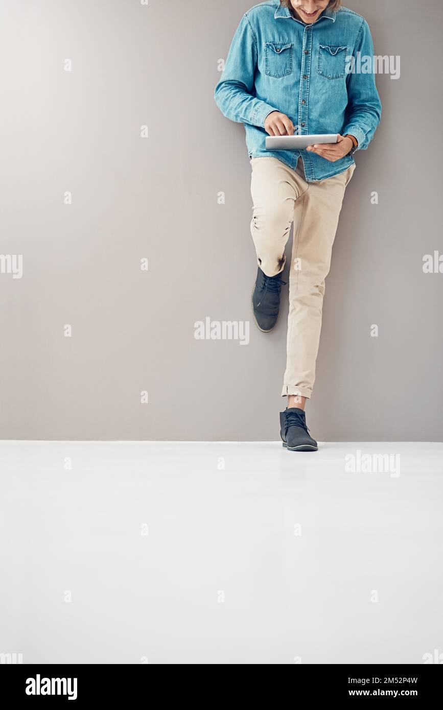 Who says business has to be serious. an unidentifiable young entrepreneur using his tablet while leaning against a wall in the office. Stock Photo