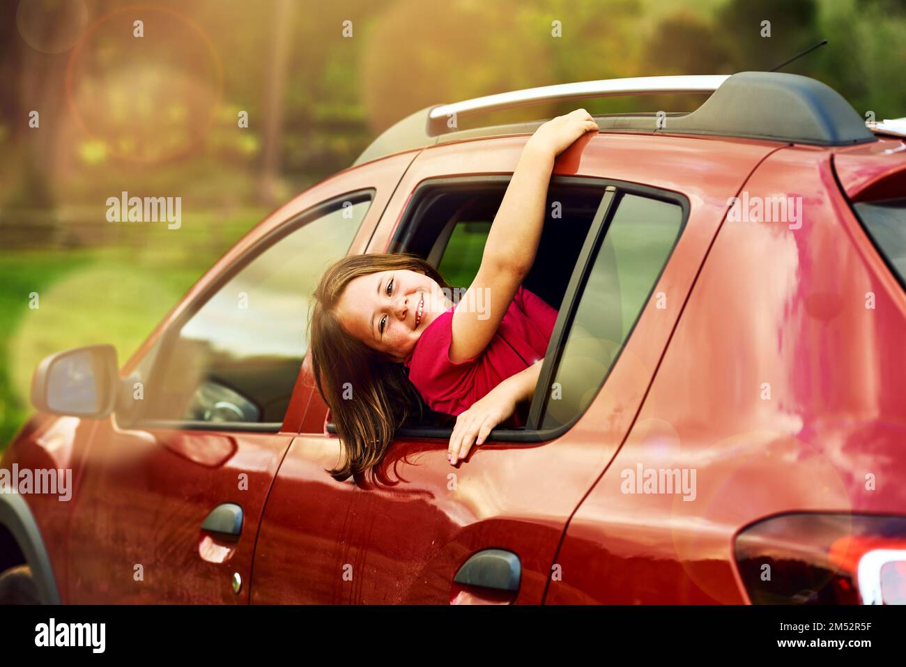 Getting a little restless in the back seat. Portrait of an adorable little girl leaning out of a car window outside. Stock Photo