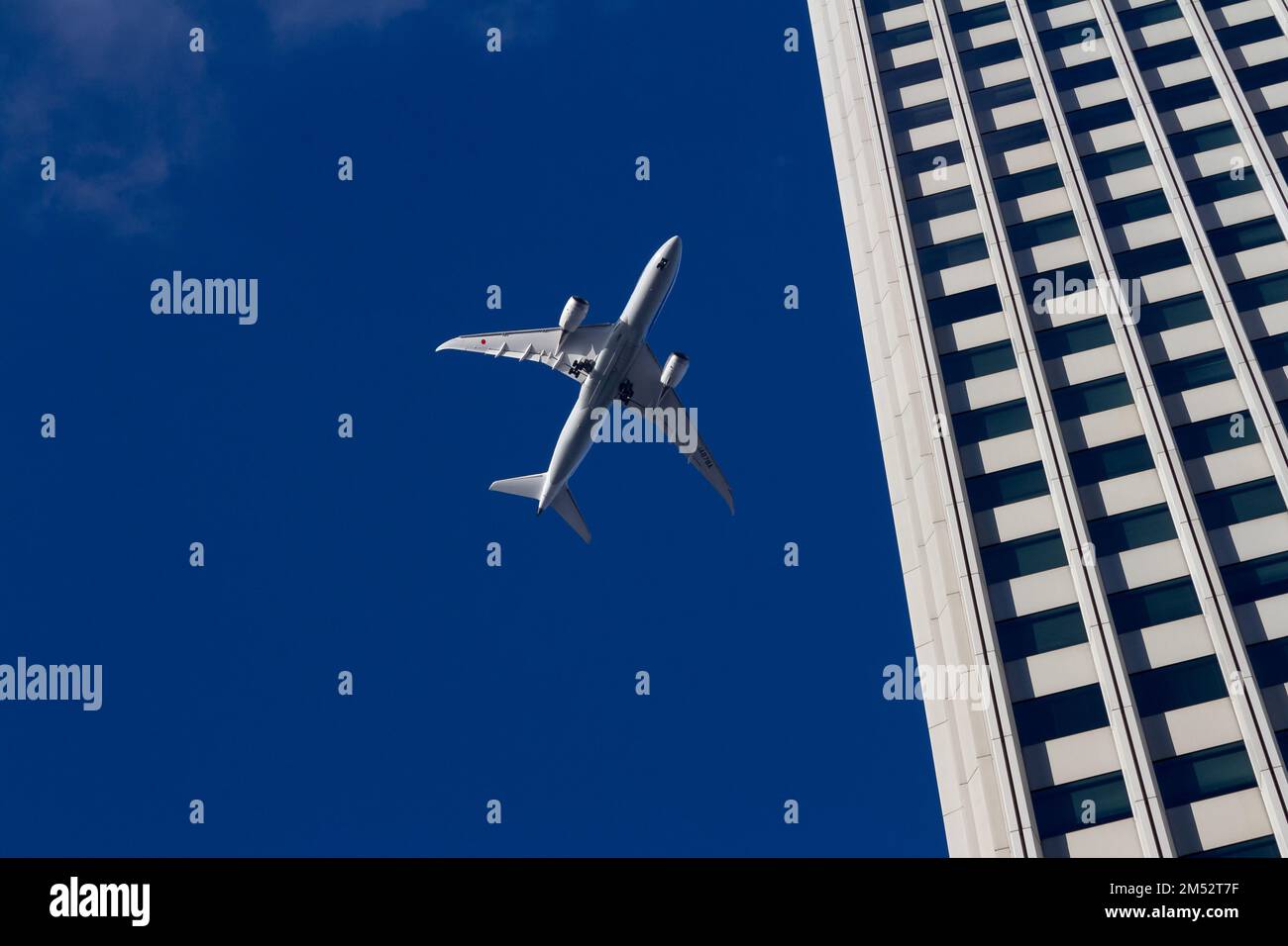 The underside of an All Nippon Airways (ANA) Boeing 787-8 Dreamliner passenger jet flying dramatically low over a building in Tokyo, Japan. Stock Photo