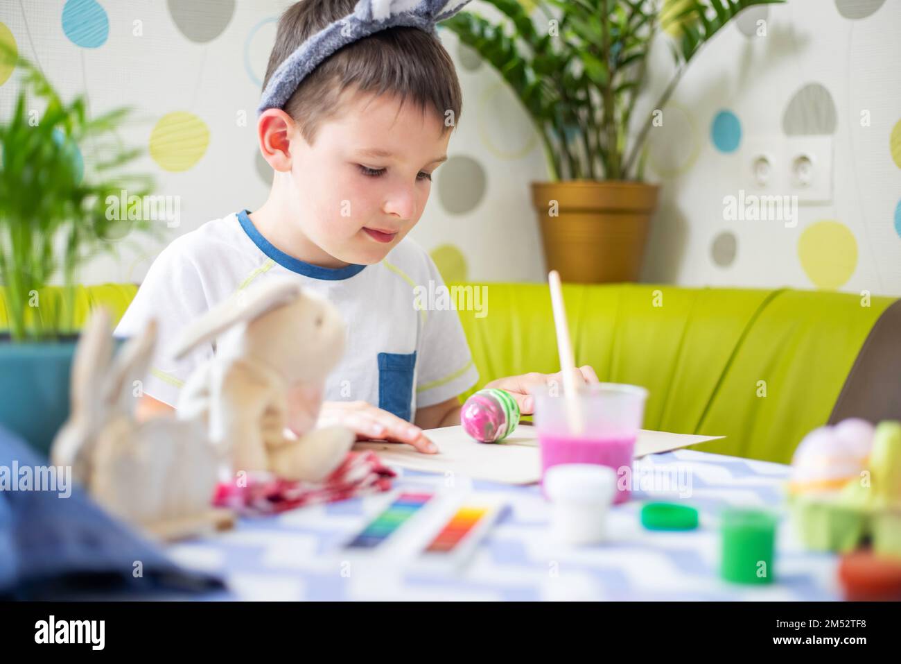 Happy Easter. Boy in bunny ears dyes colorful egg for Easter hunt Stock Photo