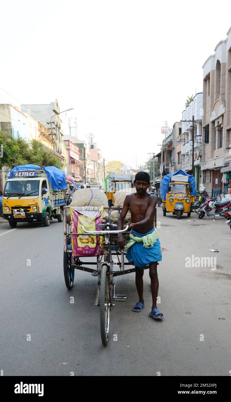 A Tamil man dressed in lungi pushing his loaded transport rickshaw in central Madurai, Tamil Nadu, India. Stock Photo