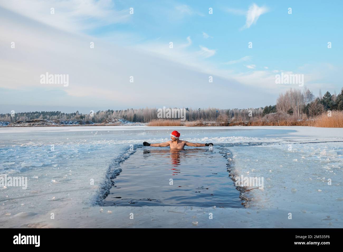 Young man in Santa's hat swimming in an ice cold water surrounded by ice. Stock Photo