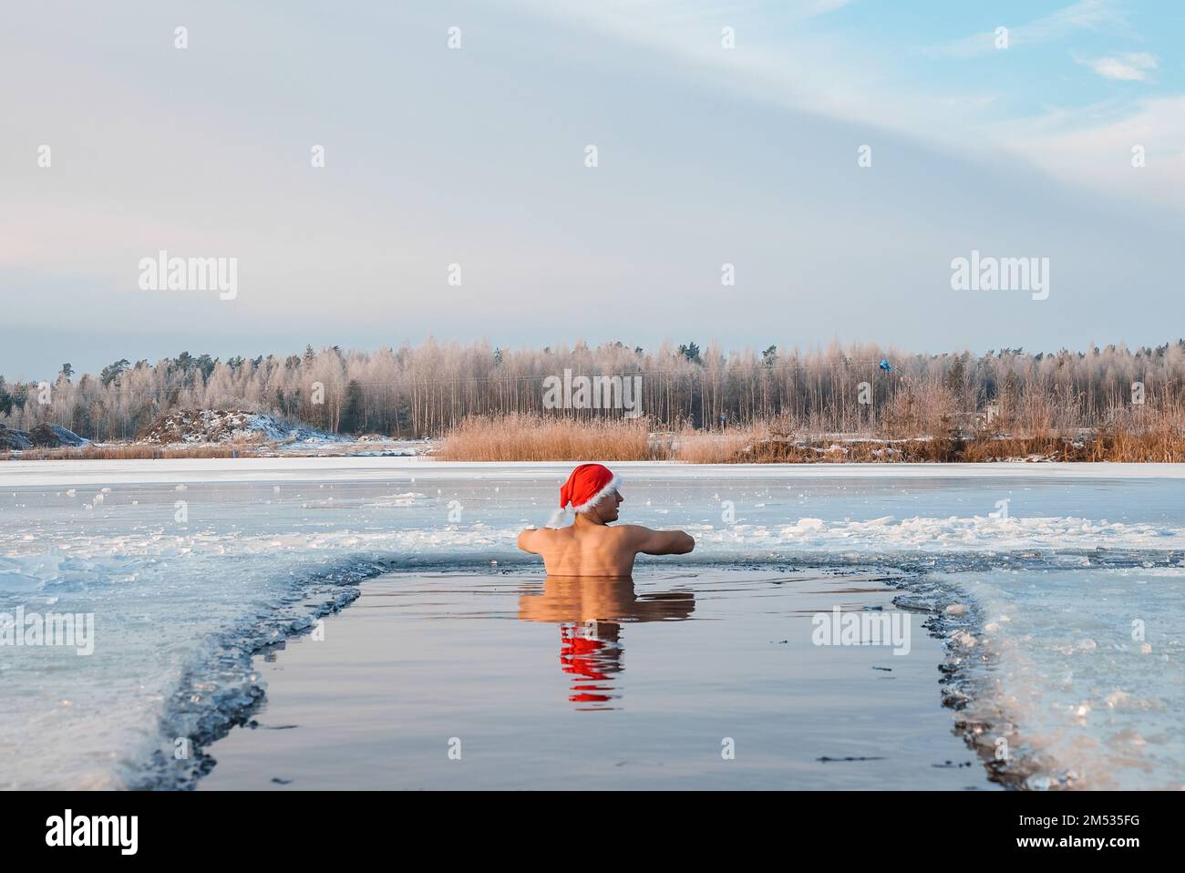 Young man in Santa's hat swimming in an ice cold water surrounded by ice. Stock Photo