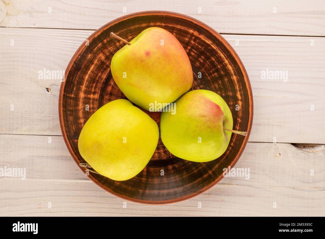 Three sweet green apples with a clay plate on a wooden table, macro, top view. Stock Photo