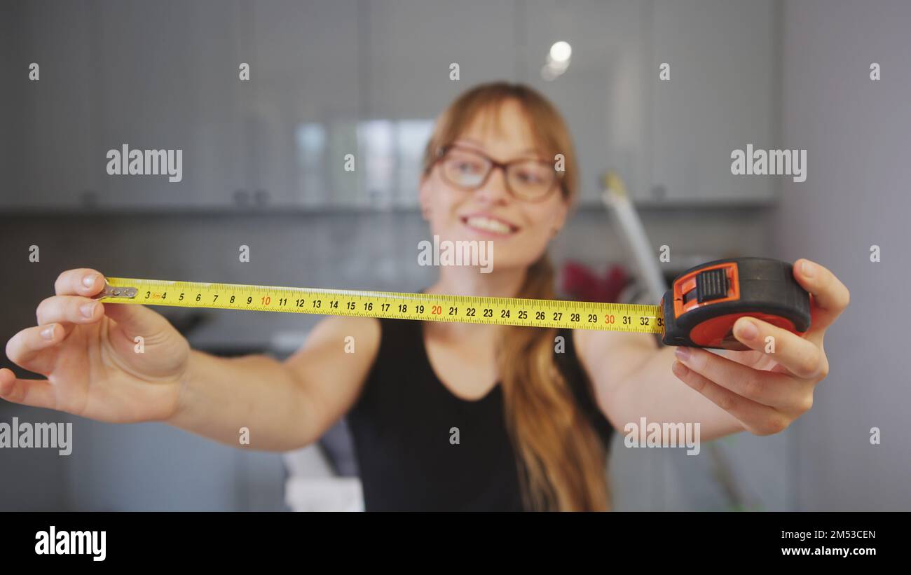 Beautiful woman carpenter using measure tape in his kitchen. Showing measure tape in front of the camera. High quality photo Stock Photo