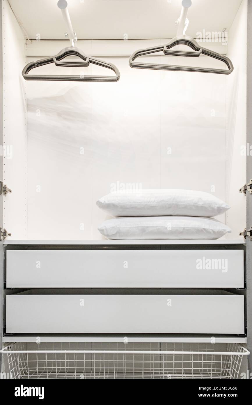 Interior of an open closet with white doors, shirt racks, white pillows, drawers and a pull-out wire basket Stock Photo