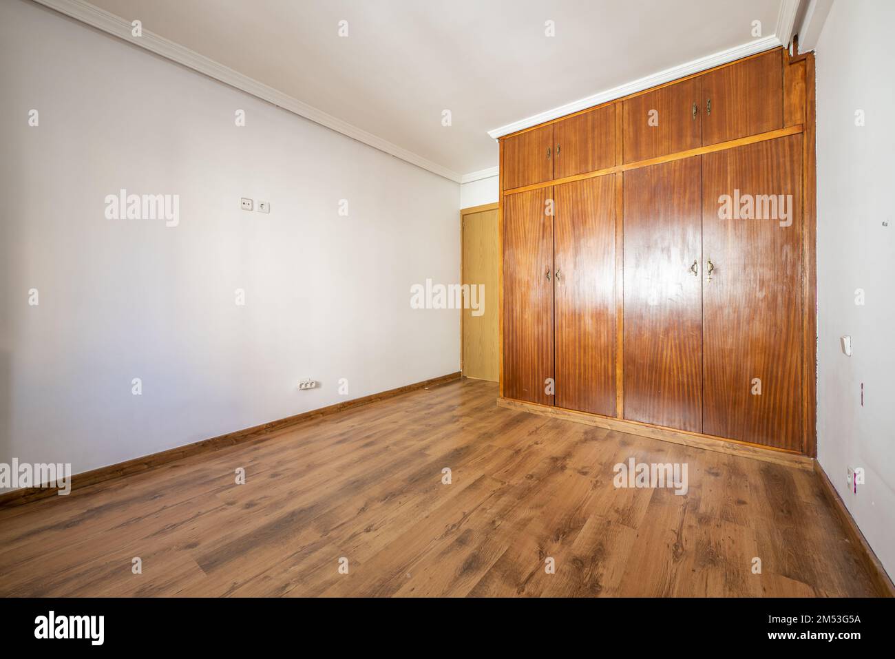 Empty room with built-in wooden wardrobe with 4 sapele wood doors and laminated flooring Stock Photo