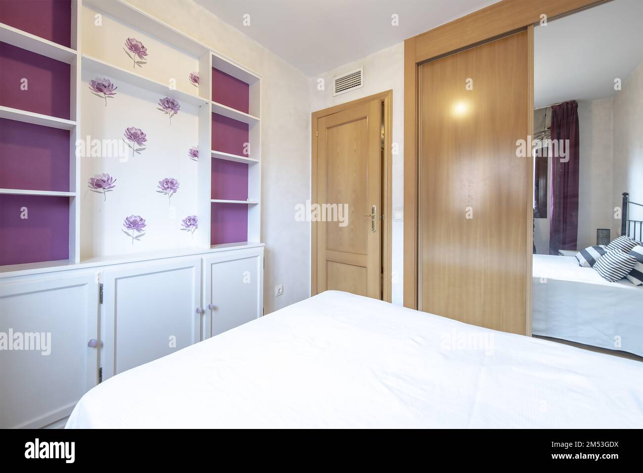 Bedroom with a double bed with a white wooden shelf with doors and a