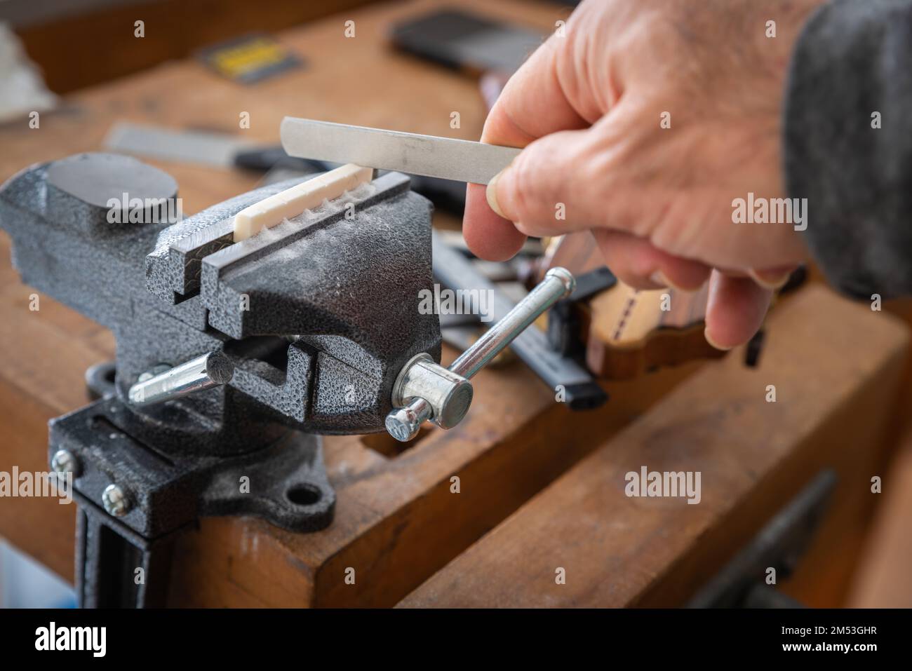 Musical instrument guitar repair and service - worker hand uses file to repair guitar bone nut placed on guitar neck. Stock Photo