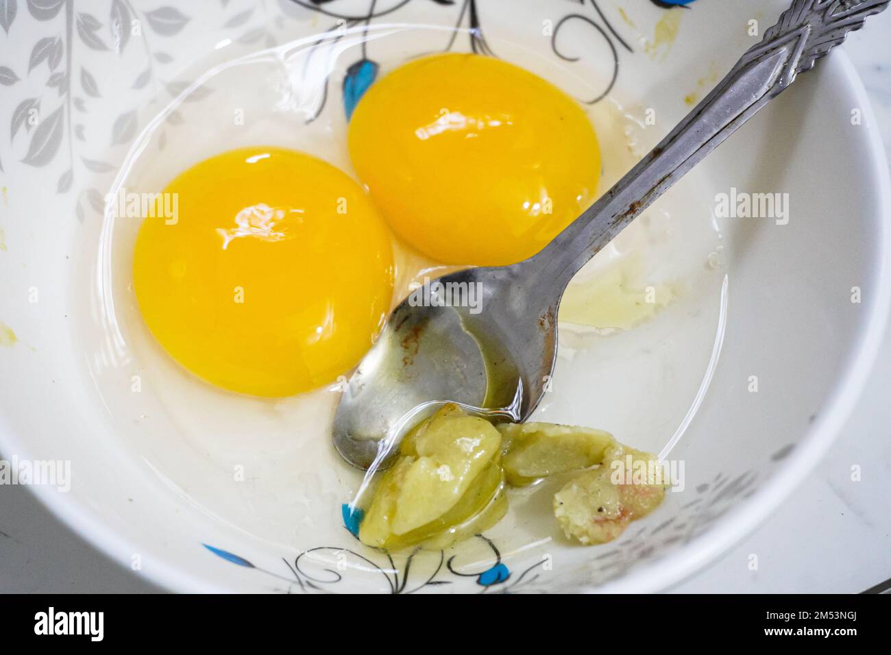 Top view of two raw eggs yolk in bowl with a steel spoon. Stock Photo