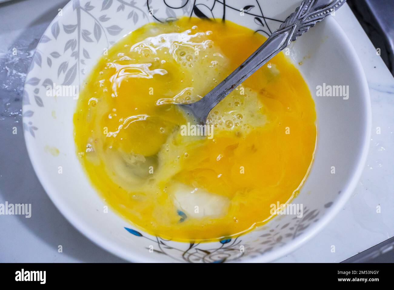 Top view of two raw eggs crucked yolk in bowl with a steel spoon Stock