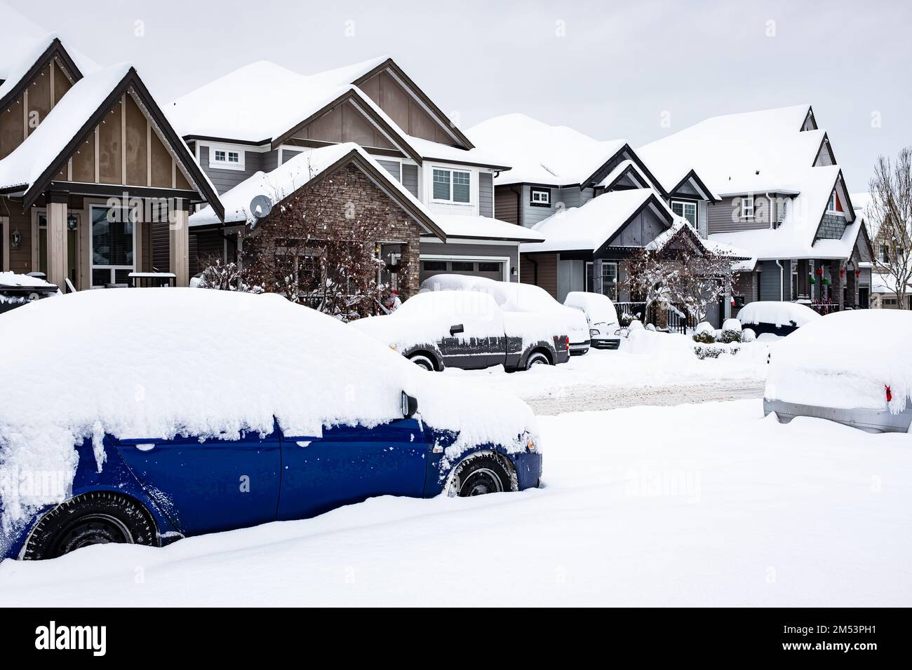 A car under the snow. Winter urban scene in Canada. Vehicles covered with snow in the winter blizzard in the parking. Cars in snowdrifts after a snowf Stock Photo