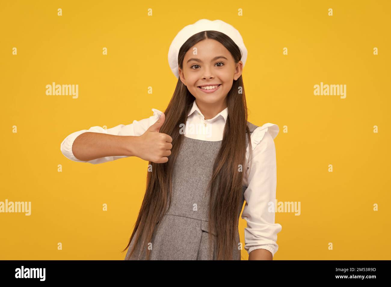 Happy casual teenager child girl showing thumb up and smiling isolated on yellow background. Happy girl face, positive and smiling emotions. Stock Photo