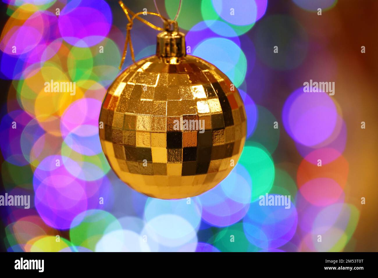 New Year toy, golden mirror ball hanging on blurred festive lights background. Christmas decorations in winter holidays Stock Photo