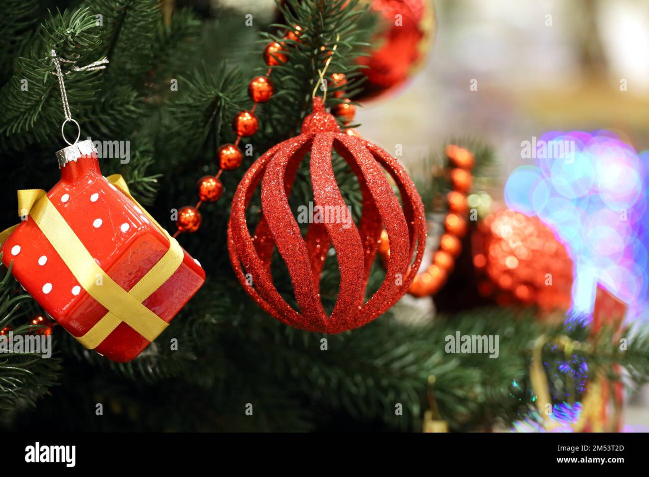 New Year toys on Christmas tree. Red ball and gift box hanging on blurred festive lights background Stock Photo