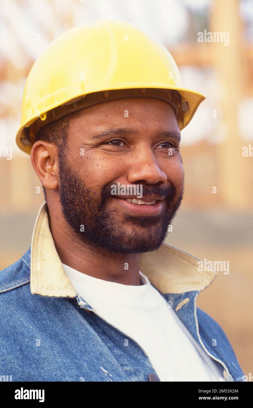 African-American man with a beard and a hardhat on a construction site glancing off into the distance Stock Photo