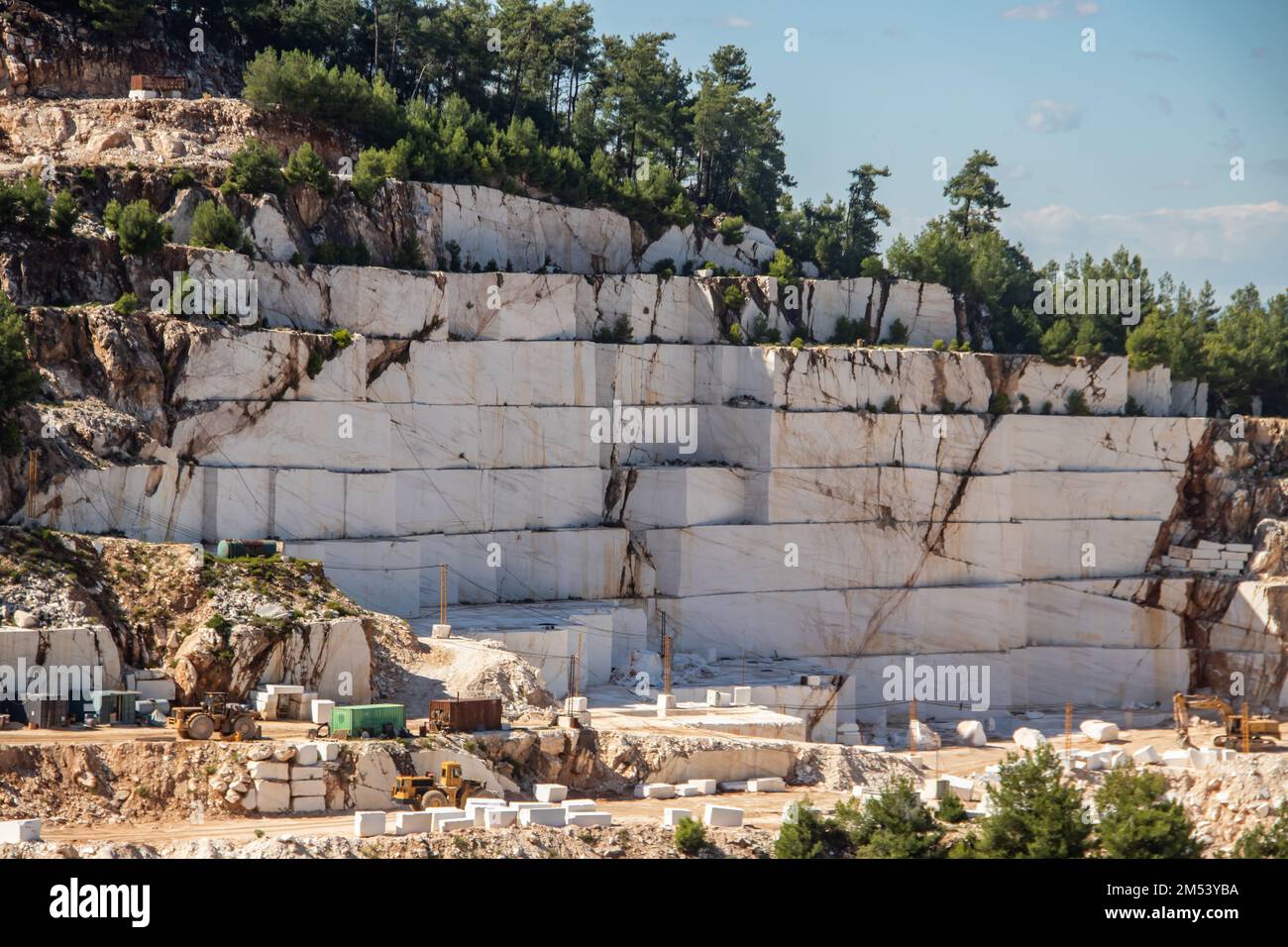 An open-pit mine of white marble stone with heavy machinery used to extract and mine the precious stone for further use and production Stock Photo