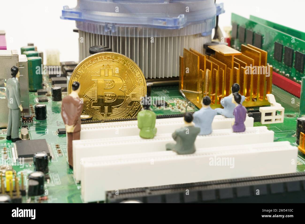 Business and technology concept. On the motherboard of the computer is a gold bitcoin coin and miniature figures of people. Figures out of focus. Stock Photo