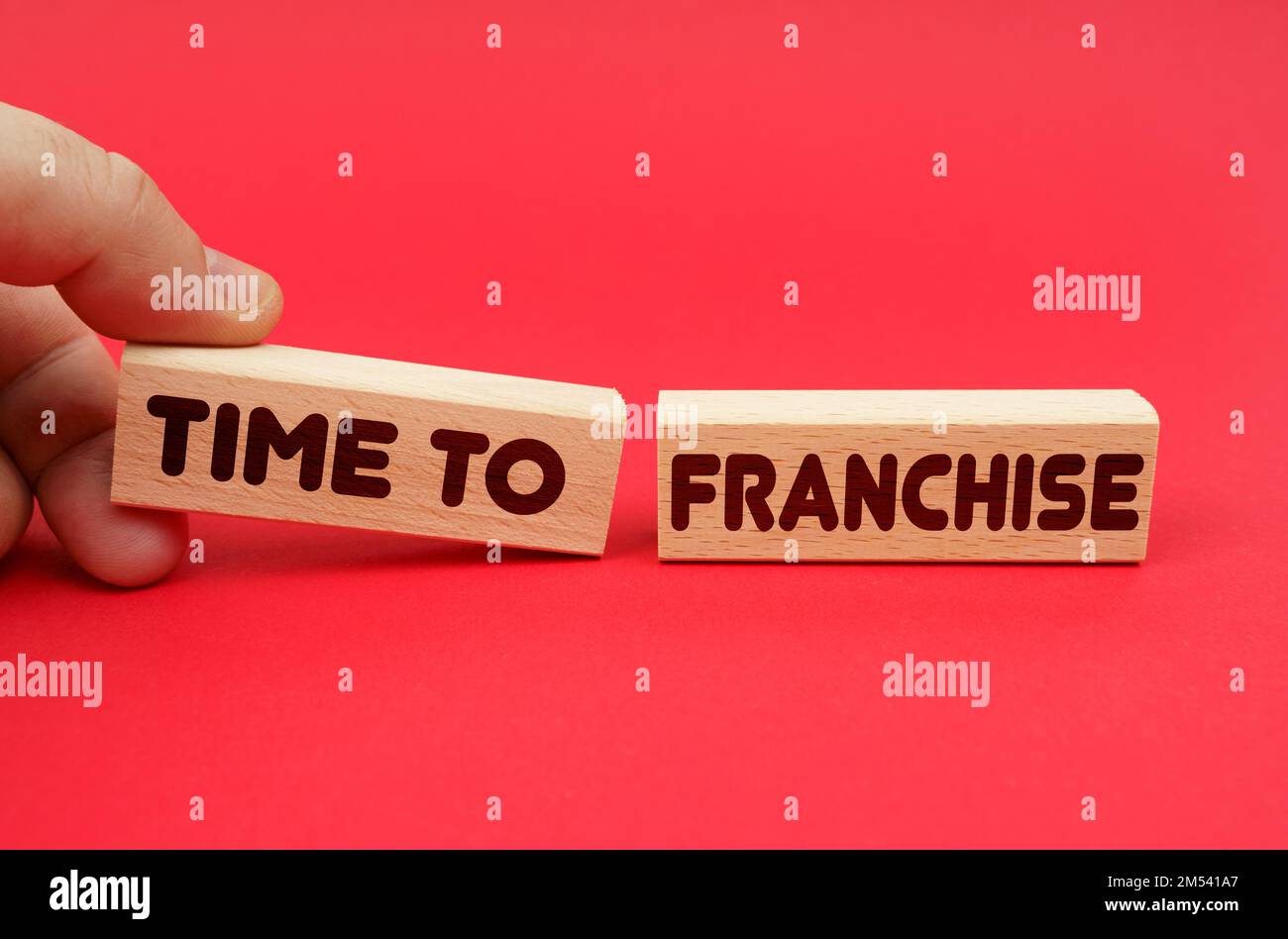 Business concept. On a red background, wooden blocks, one of them in hand. The blocks are written - Time to Franchise Stock Photo