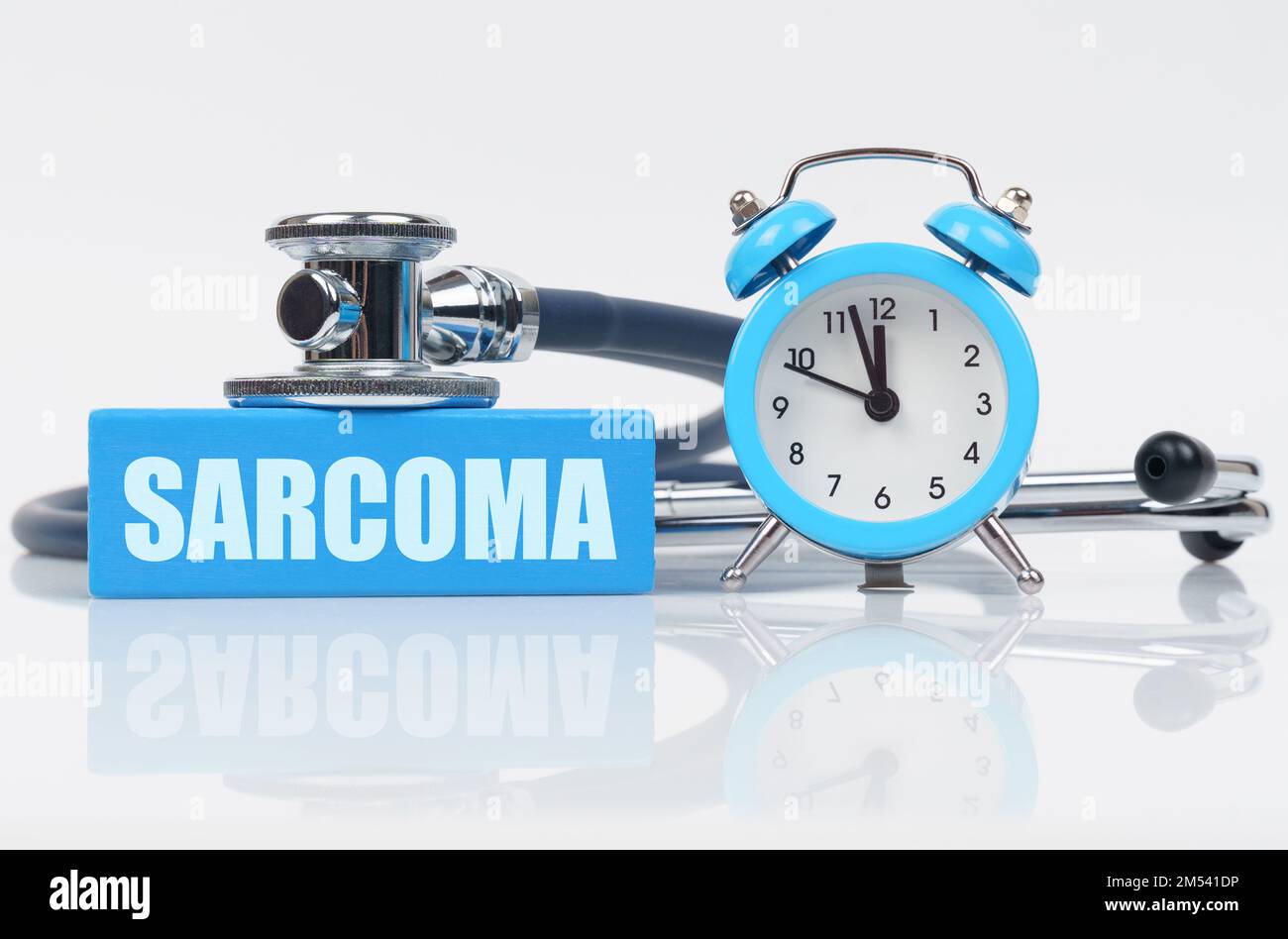Medical concept. On a white surface there is an alarm clock, a stethoscope and a blue block with the inscription - SARCOMA Stock Photo