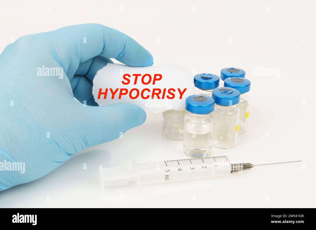 Medical concept. In the man's hand is a piece of paper with the inscription - STOP HYPOCRISY, next to it lies a syringe and injection jars. Stock Photo