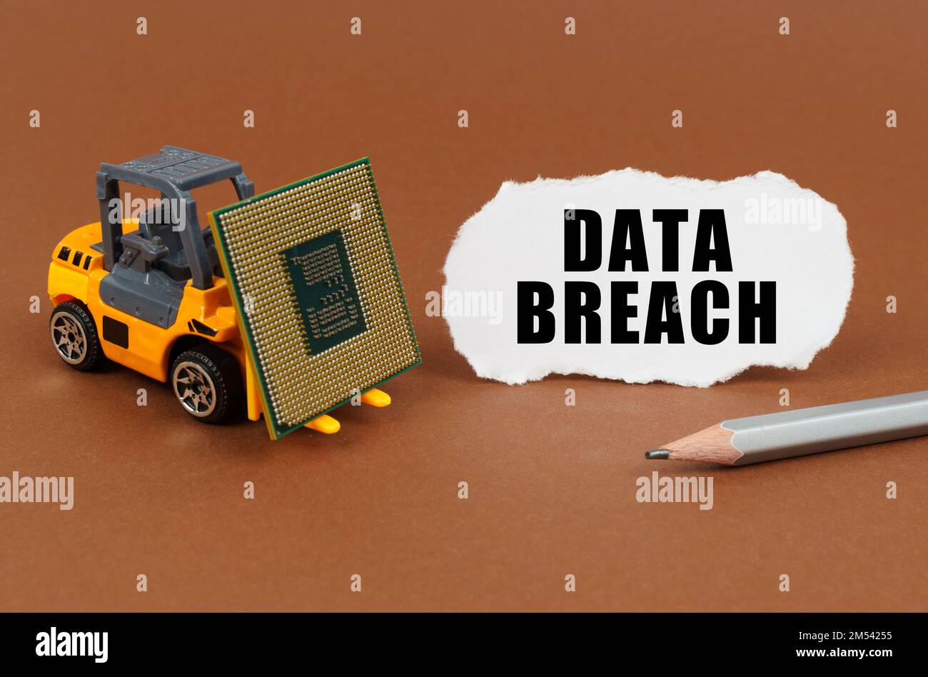 Technological concept. On a brown surface, a forklift is transporting a processor, next to it is paper with the inscription - Data Breach Stock Photo