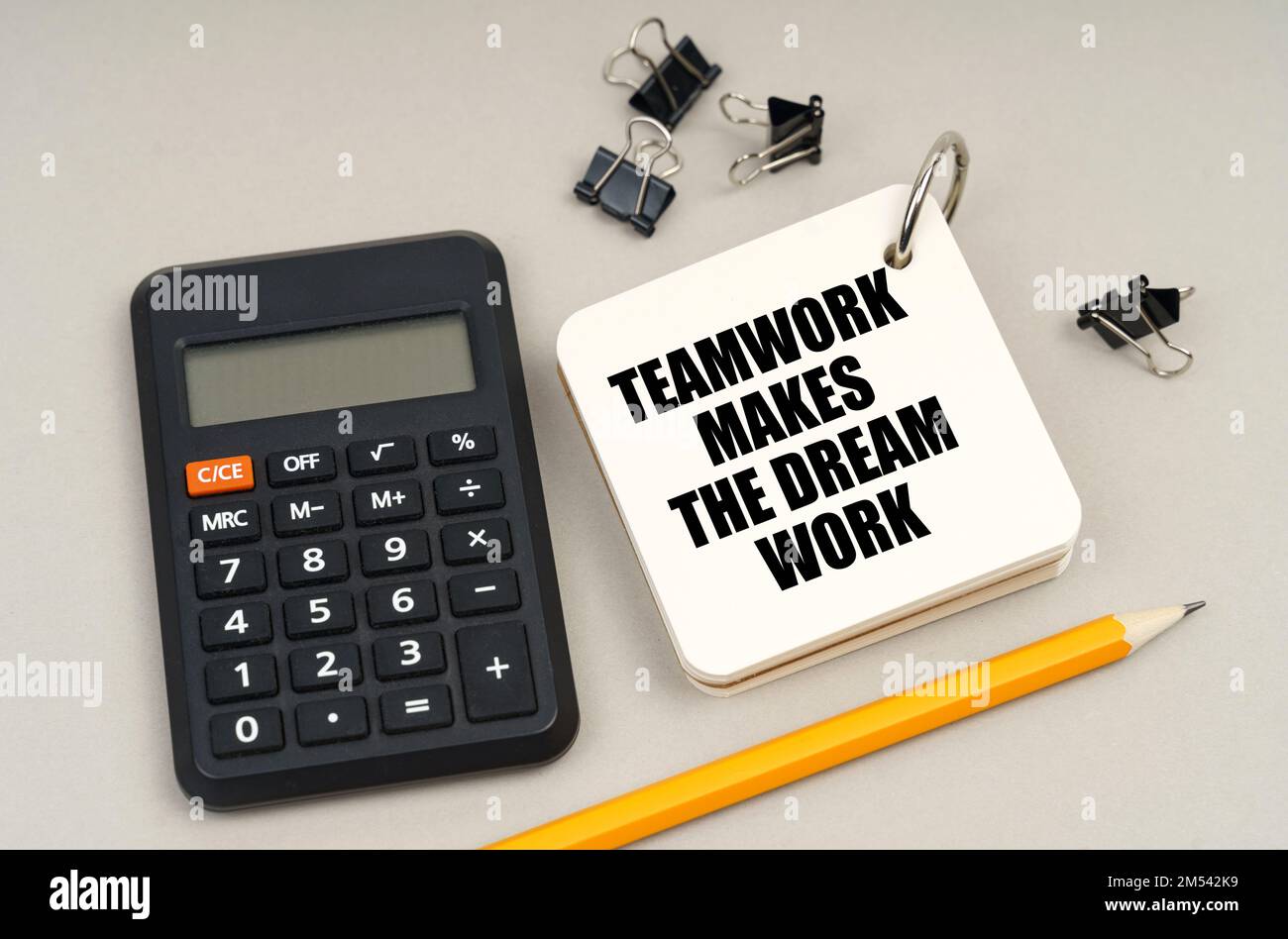 Business concept. On a gray surface, a calculator, a pencil and a notepad with the inscription - Teamwork Makes The Dream Work Stock Photo