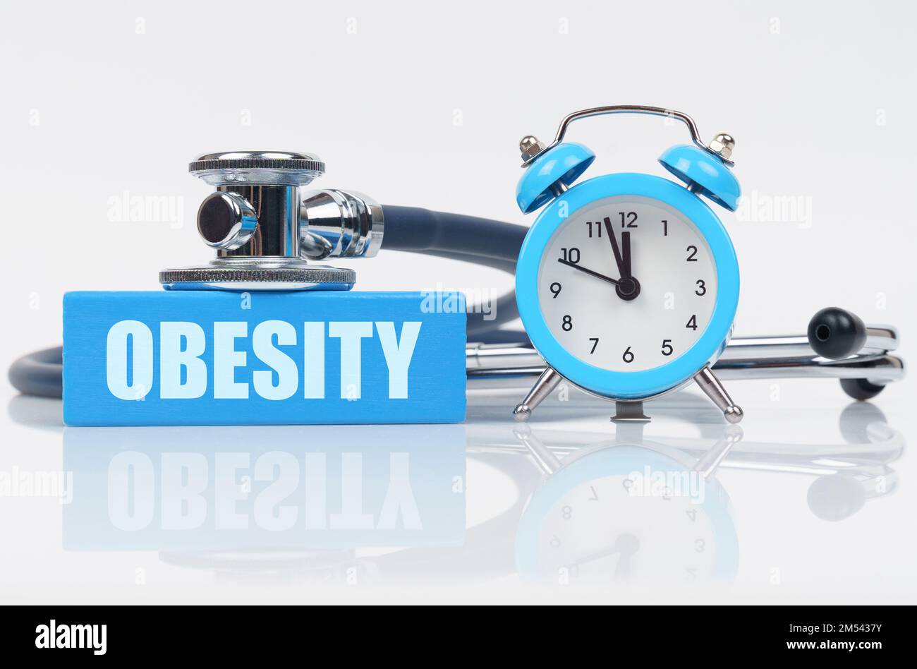 Medical concept. On a white surface there is an alarm clock, a stethoscope and a blue block with the inscription - OBESITY Stock Photo