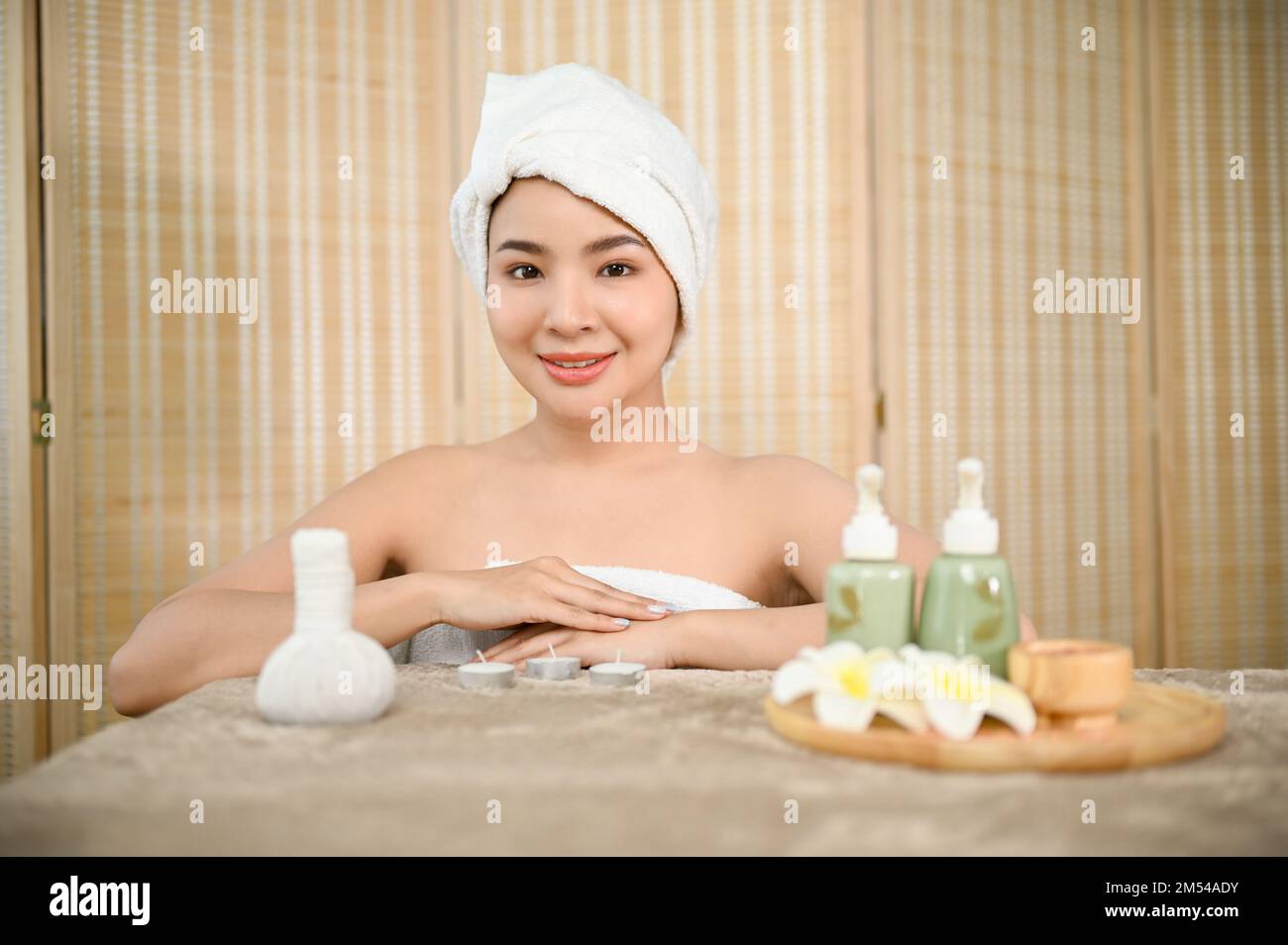 Attractive and beautiful young Asian woman in bathrobe with herbal massage ball, treatment body oil bottle, and salt body scrub, getting body treatmen Stock Photo