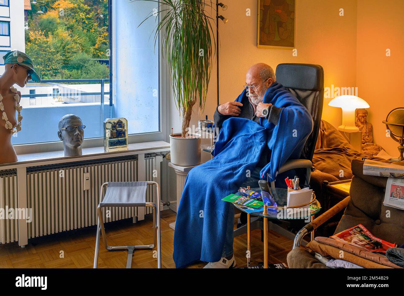 Old man wrapped in blankets, save energy, freeze because of Putin, save heating costs, low room temperature, Bavaria, Germany Stock Photo