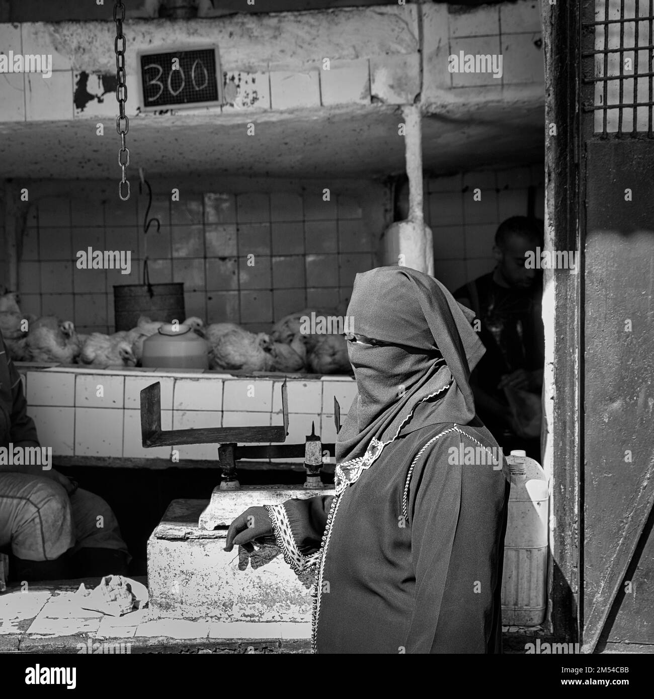 Traditionally dressed Muslim woman with niqab stands at poultry stall, market stall, black and white image, symbolic image, Morocco Stock Photo