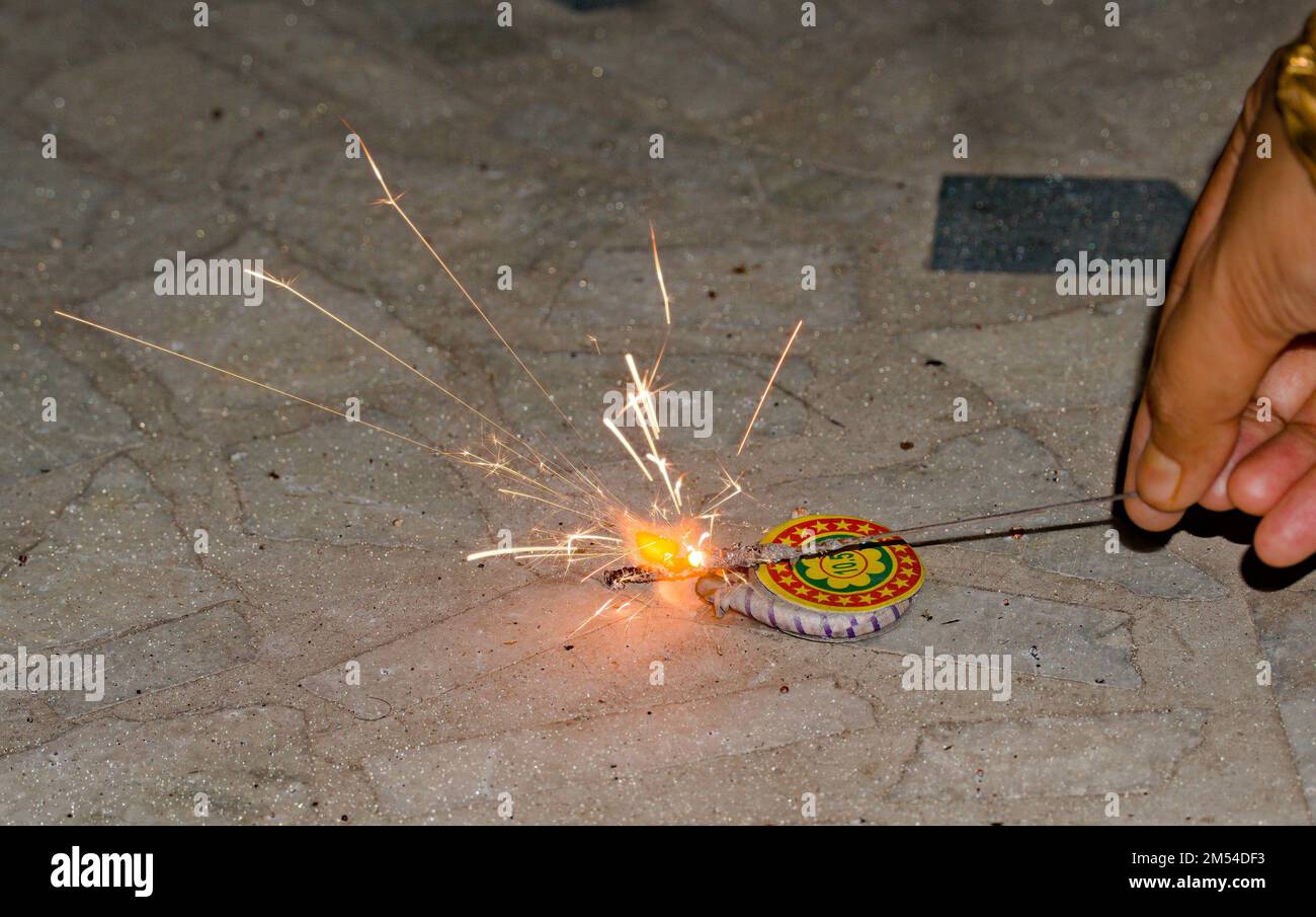 igniting ground spinner with the help of sparkler during diwali. Stock Photo
