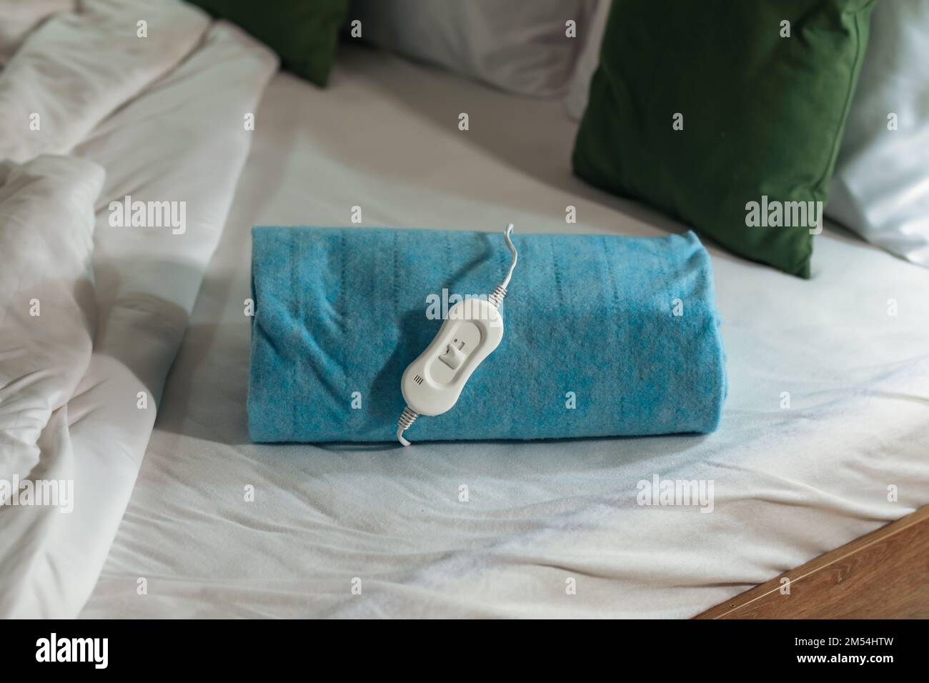 Folded electric heating pad with controller on bed at night, closeup Stock Photo