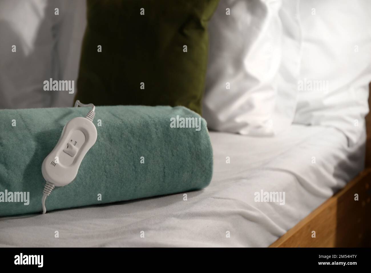 Folded electric heating pad with controller on bed at night, closeup Stock Photo