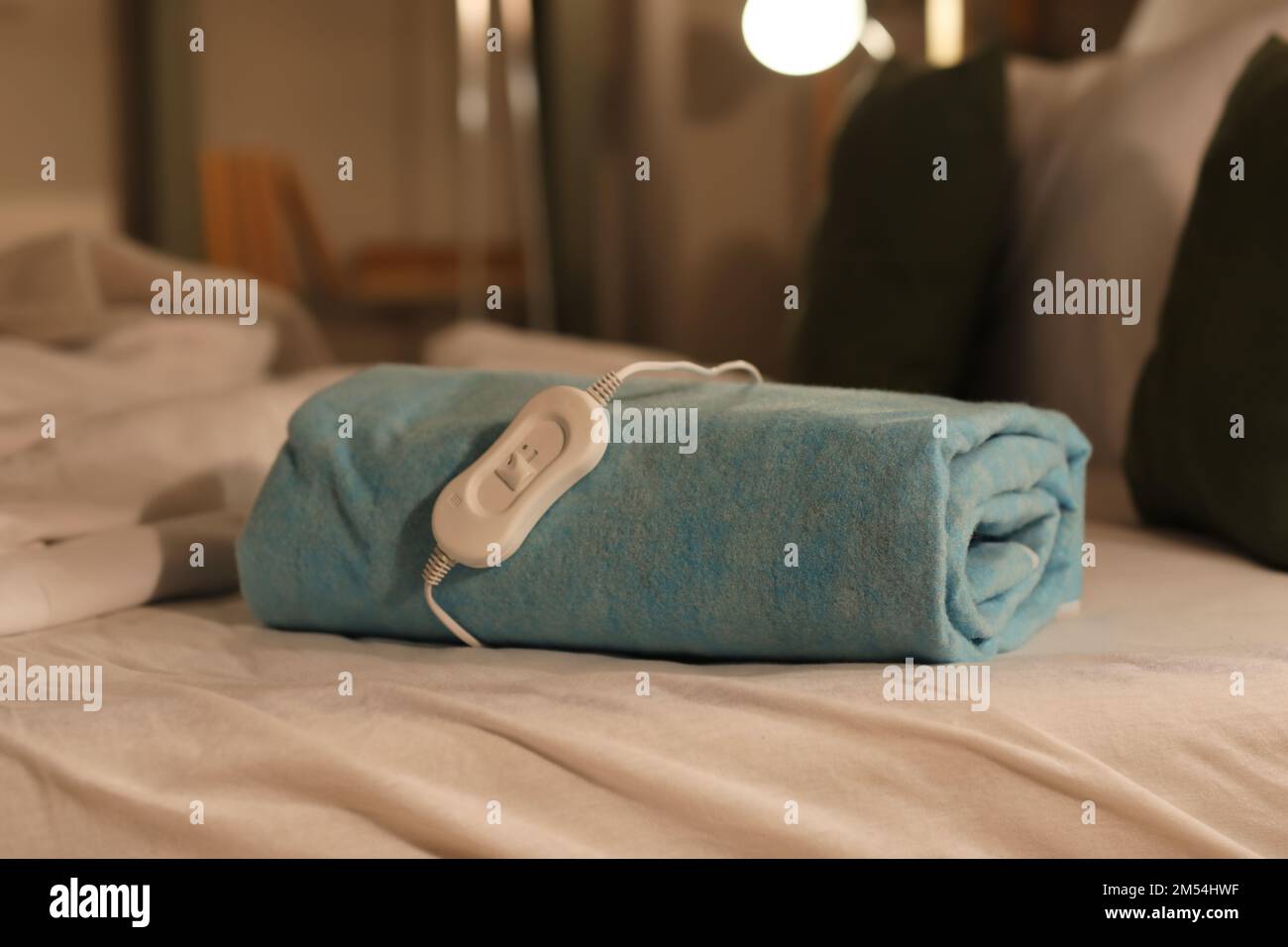 Folded electric heating pad with controller on bed at night, closeup Stock Photo