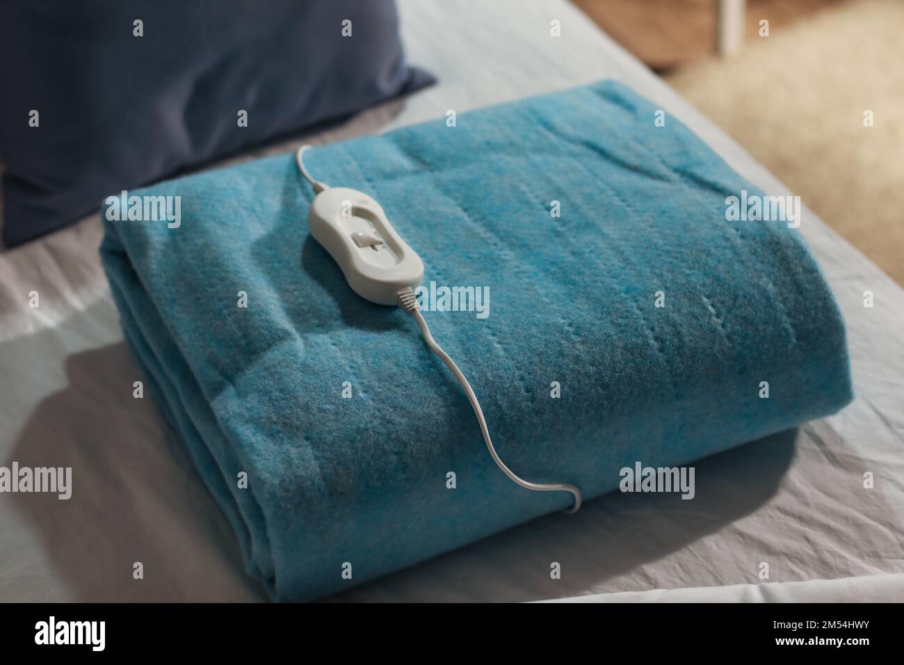 Folded electric heating pad with controller on bed at night, closeup Stock Photo