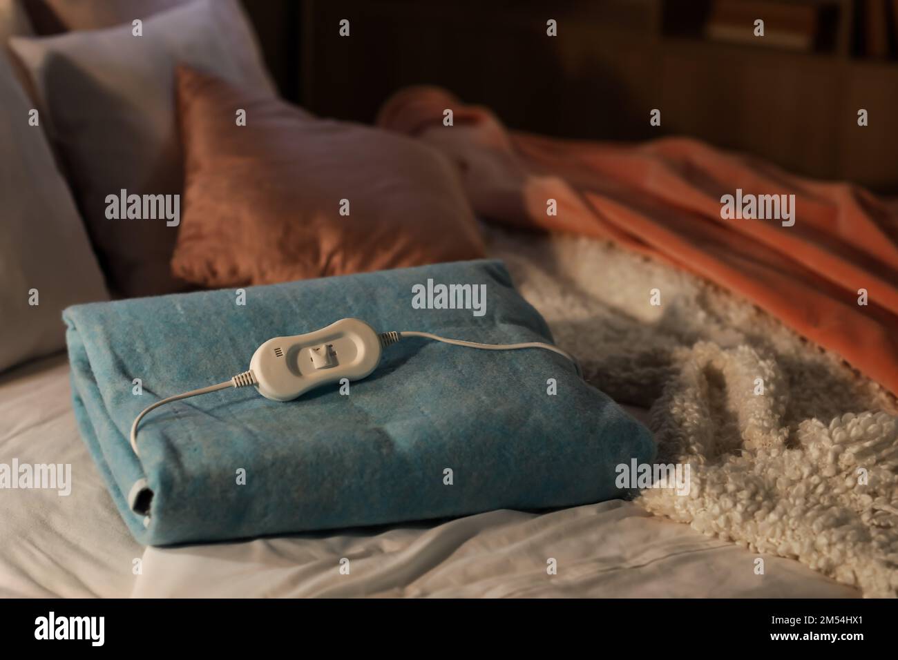 Folded electric heating pad with controller on bed at night, closeup Stock Photo