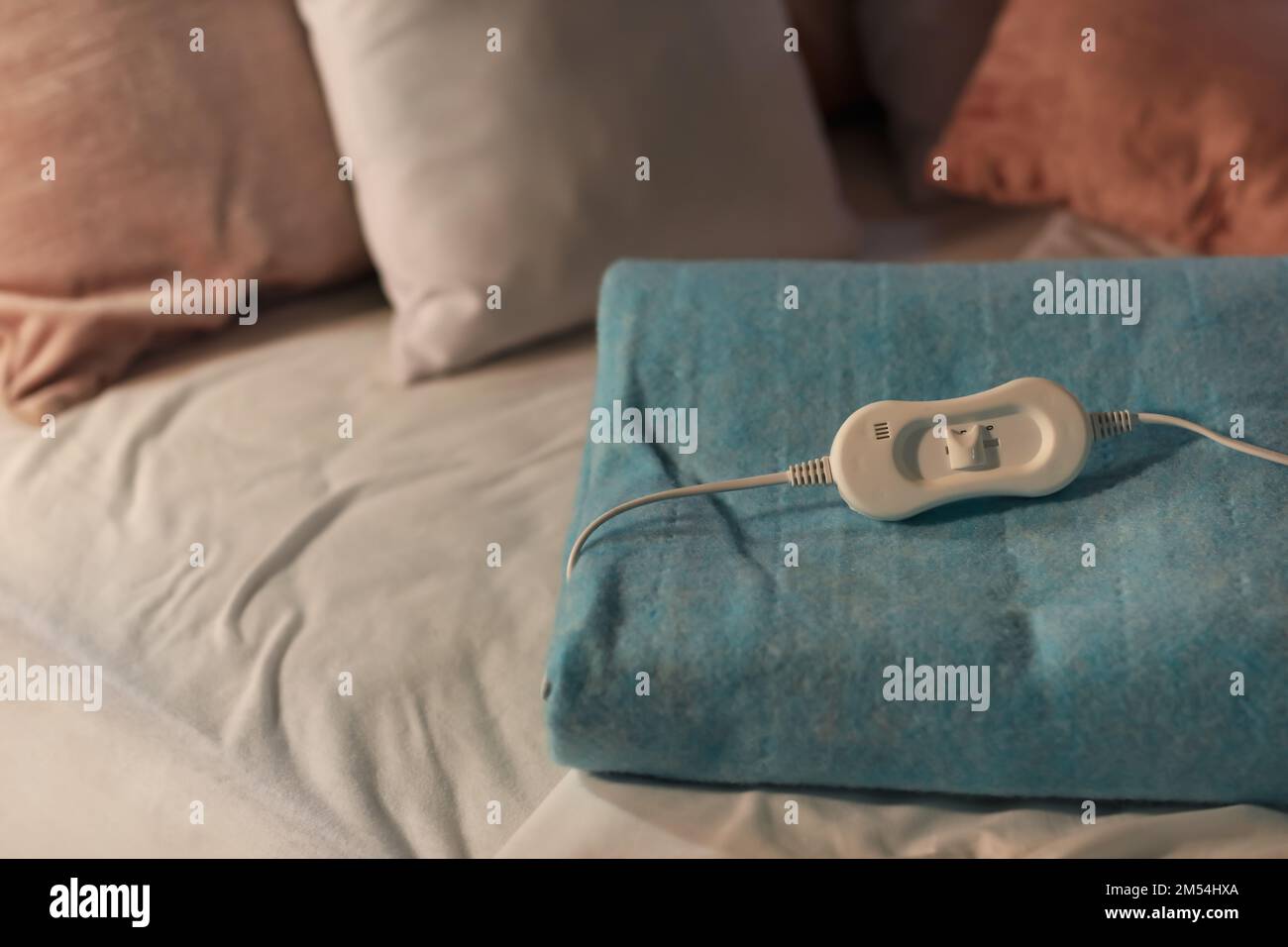 Folded electric heating pad with controller on bed at night, closeup Stock Photo