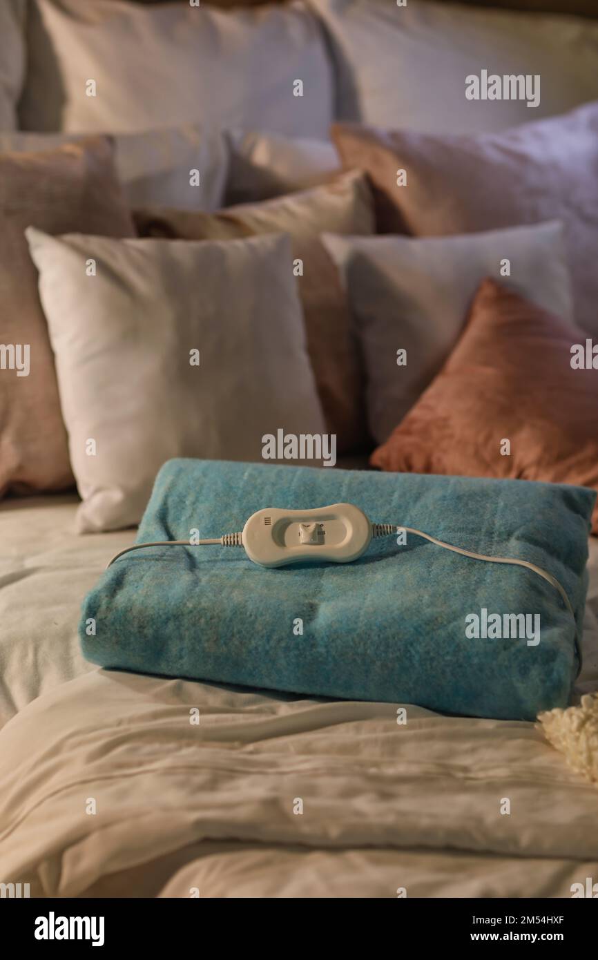 Folded electric heating pad with controller on bed at night, closeup Stock Photo