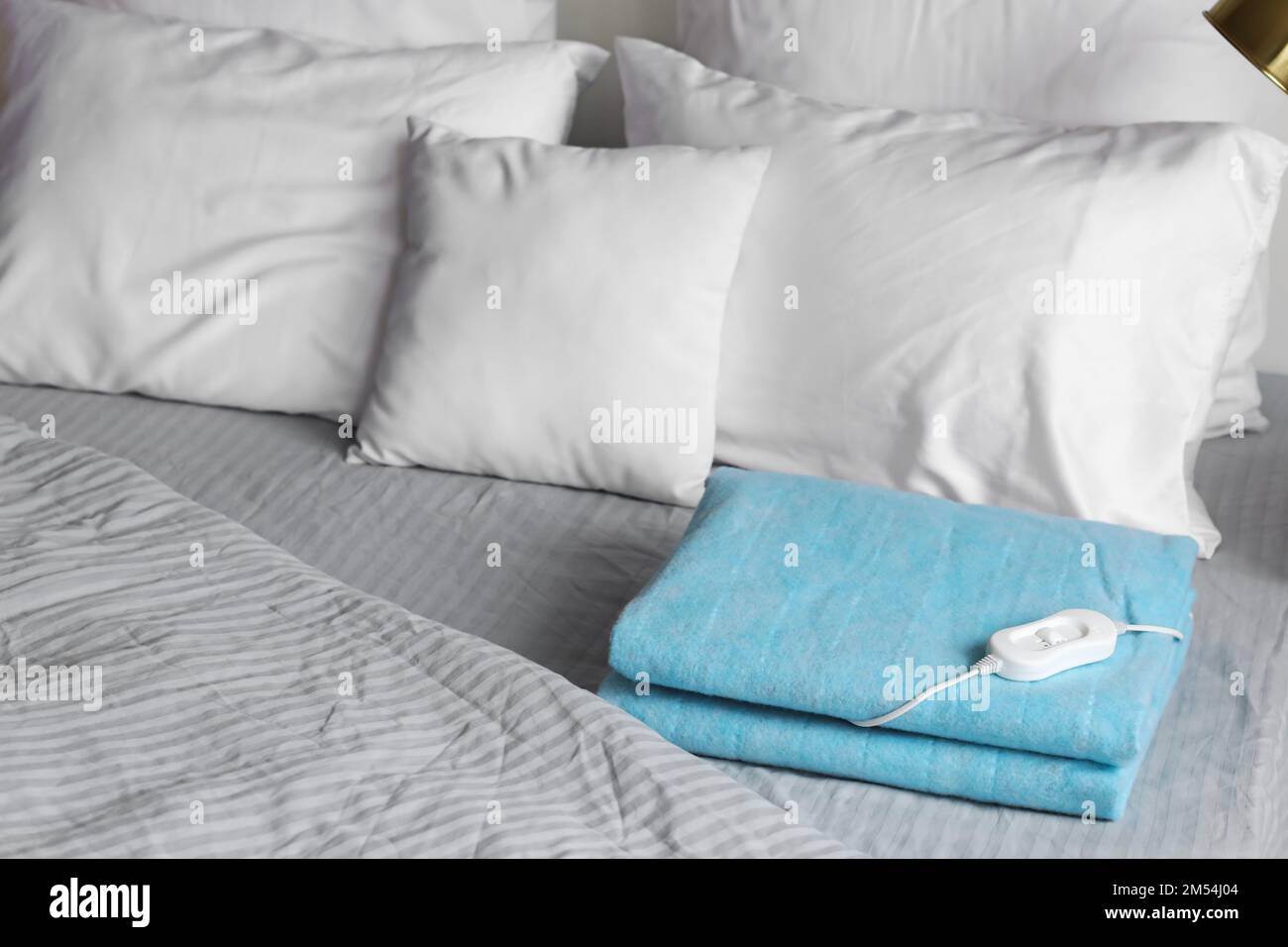 Folded electric heating pad with controller on bed in bedroom Stock Photo