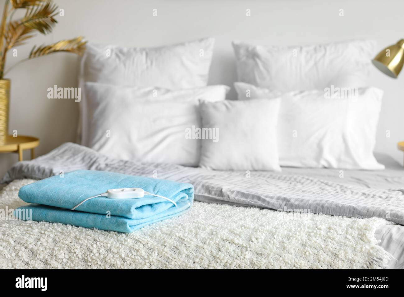 Folded electric heating pad with controller on bed in bedroom Stock Photo