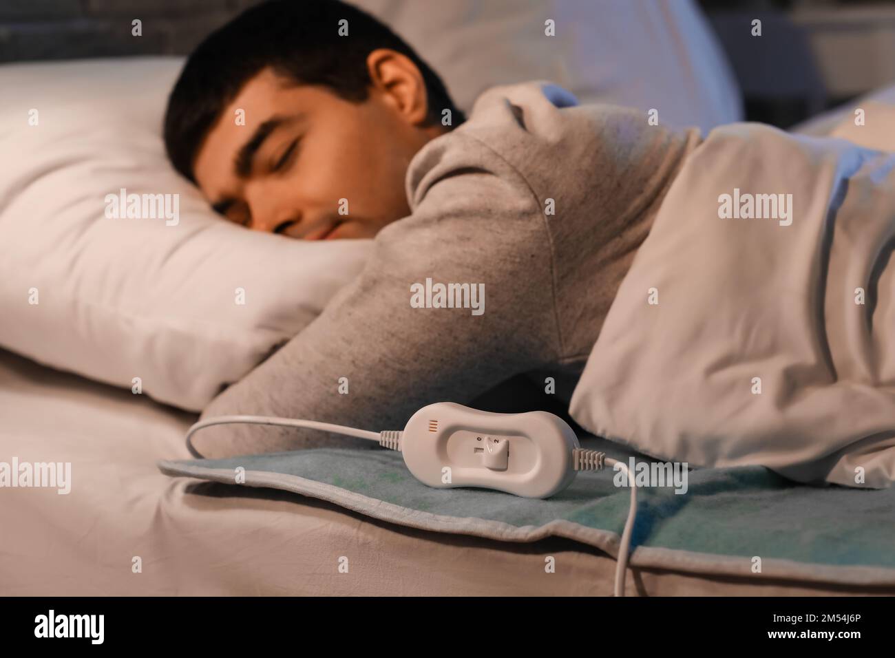 Young man sleeping on electric heating pad in bedroom at night Stock