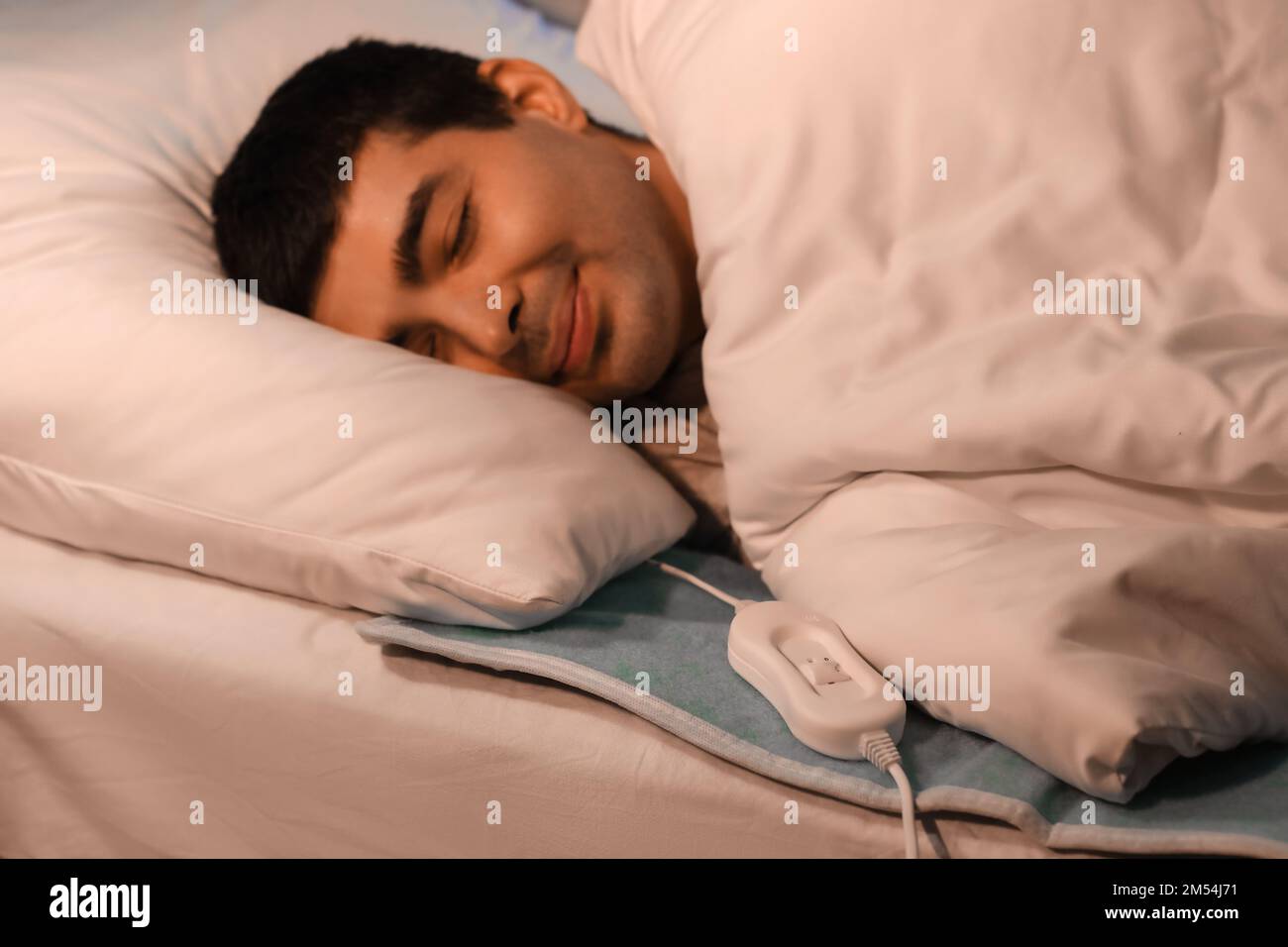Young man sleeping on electric heating pad in bedroom at night Stock
