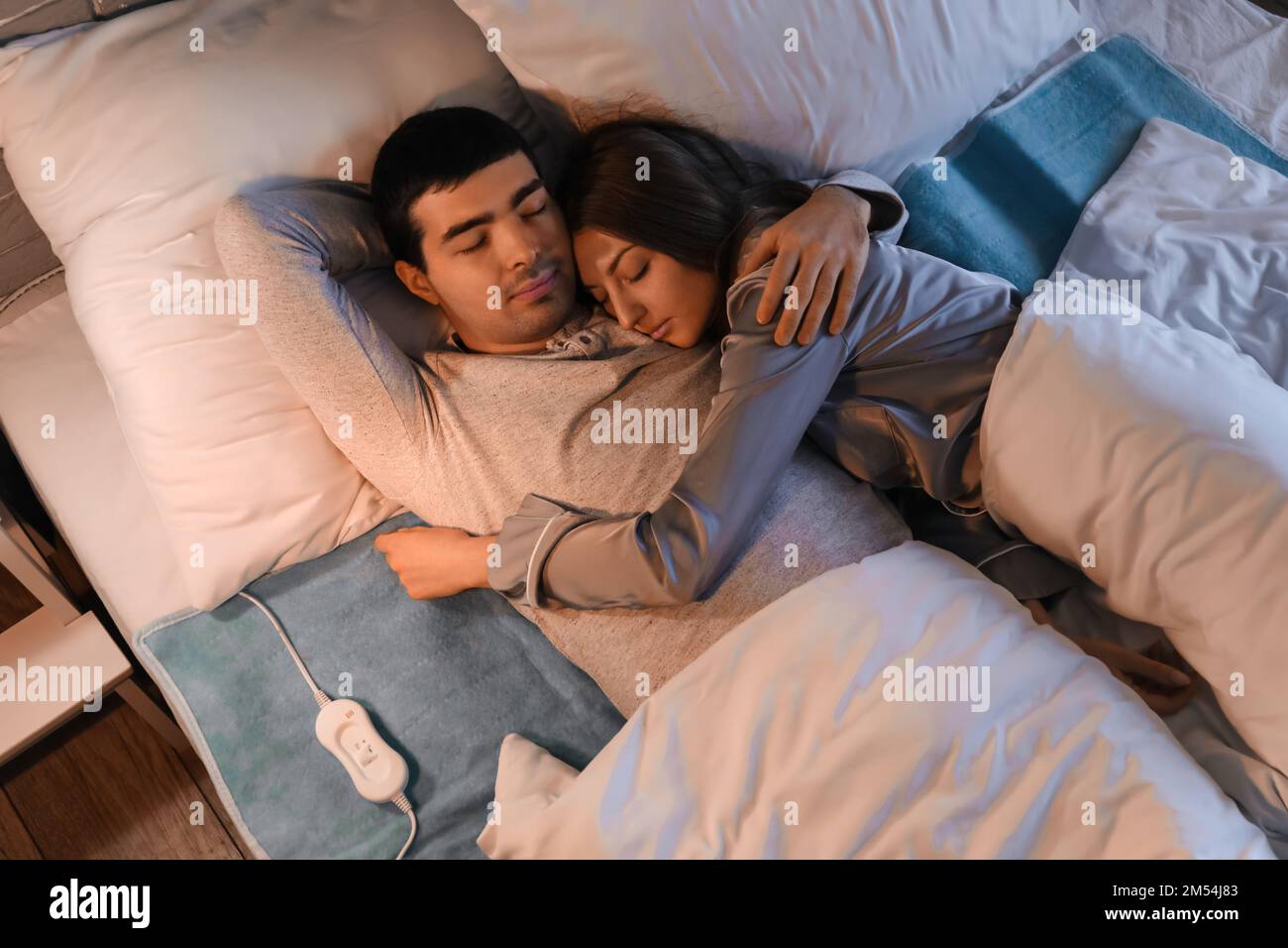 Young couple sleeping on electric heating pad in bedroom at night, top