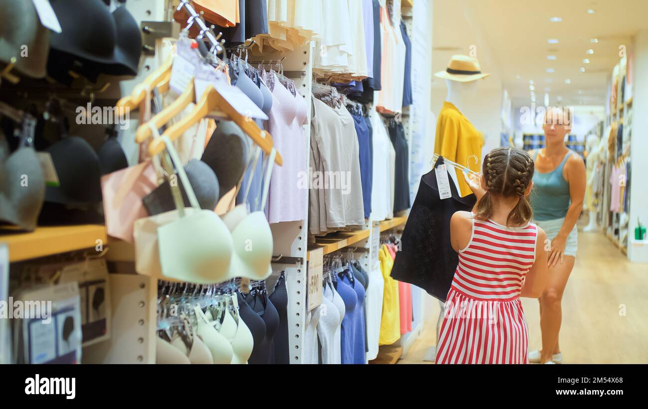 Cute shopaholic mom and daughter choose looking for clothes in clothing store. Mom and daughter shopper