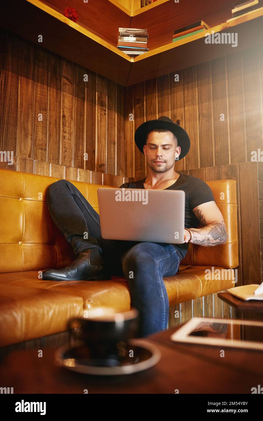 Relaxation meets productivity. a handsome young man using a laptop on a sofa in a coffee shop. Stock Photo