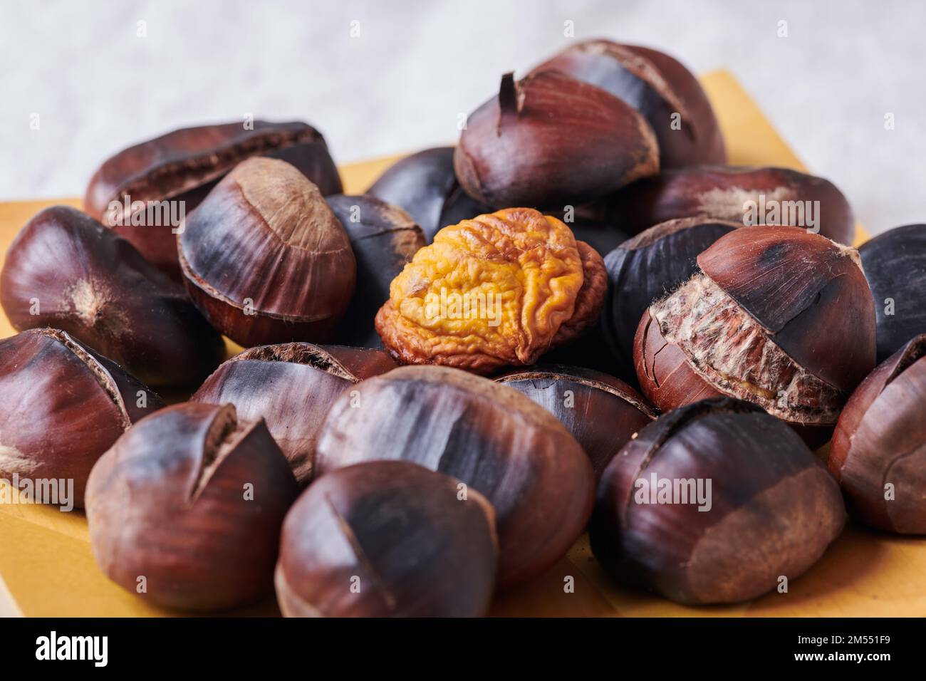 Closeup bunch of delicious roasted chestnuts with cracked shells served on lumber plate Stock Photo