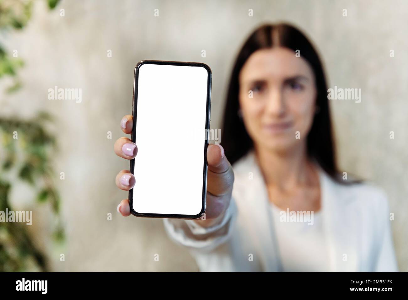 Soft focus of young female entrepreneur demonstrating cellphone with empty screen to camera during work in office Stock Photo