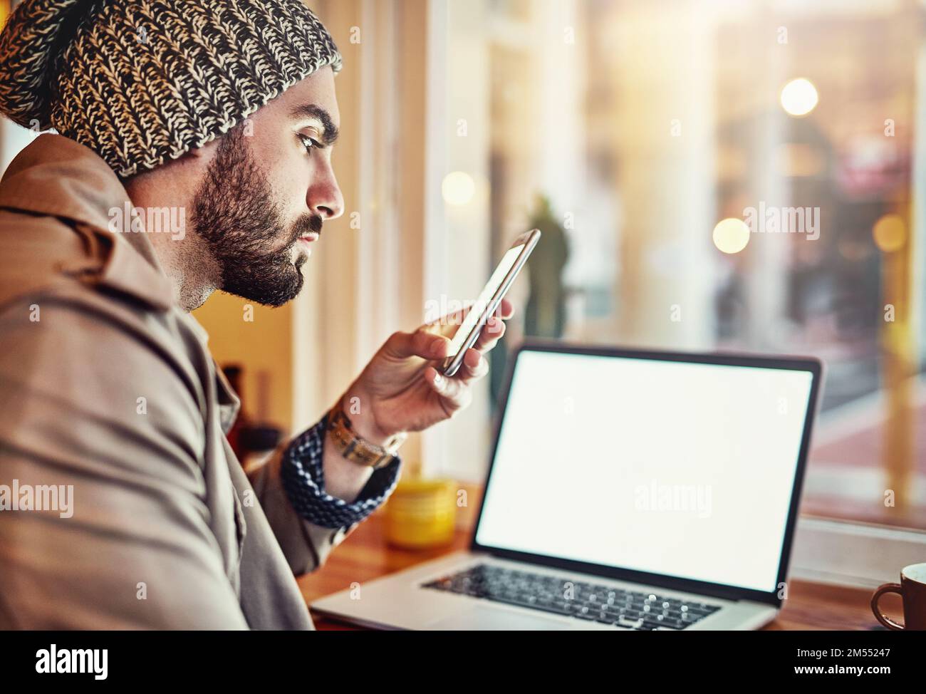 Syncing devices at his local cafe. a stylish young man reading a text message and using a laptop while sitting in a cafe. Stock Photo