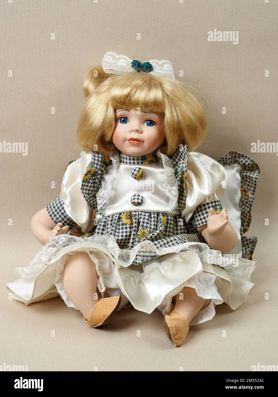 Vintage porcelain doll baby girl with blue eyes, blonde with a bow in her  hair, in a checkered sundress and a white blouse. Porcelain dolls were  popular in the 18th century in